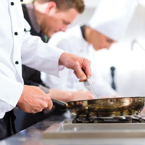 Three chefs - men and woman - in hotel or restaurant kitchen working and cooking in team